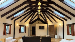 Ein geräumiges Schlafzimmer im Loft-Stil mit hohen Decken, Holzbalken, einem großen Bett, zwei Sofas und einem Fernseher.
