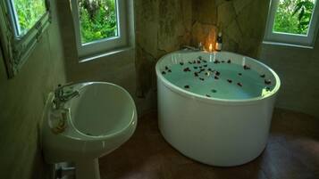 Ein Badezimmer mit einer mit Wasser und Rosenblüten gefüllten Badewanne, einem Waschbecken und einer Steinwand.