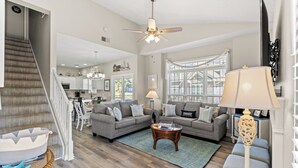 A spacious living room with a staircase, a dining area, and a kitchen in the background.