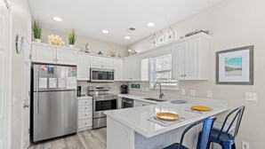 A modern kitchen with white cabinetry, stainless steel appliances, and a central island with blue bar stools.