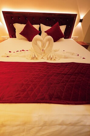 A bed with a red quilt, white pillows, and a heart-shaped towel arrangement.