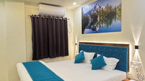 Un dormitorio moderno con una cama grande, ventilador de techo, aire acondicionado en la pared, mesita de noche con lámpara y un cuadro de un paisaje montañoso.