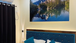 Un dormitorio con una cama grande, un ventilador de techo, un aire acondicionado instalado en la pared, una lámpara fijada a la pared y un cuadro de un paisaje montañoso.