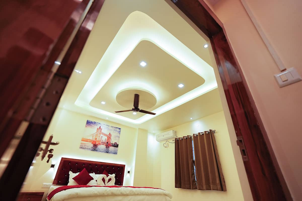 A bedroom with a modern ceiling design, a bed with a red headboard, and a painting of a bridge.