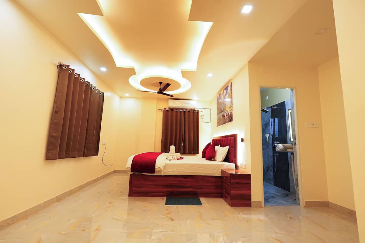 A hotel room with a bed, a ceiling fan, an air conditioning unit, and a bathroom visible through an open door.