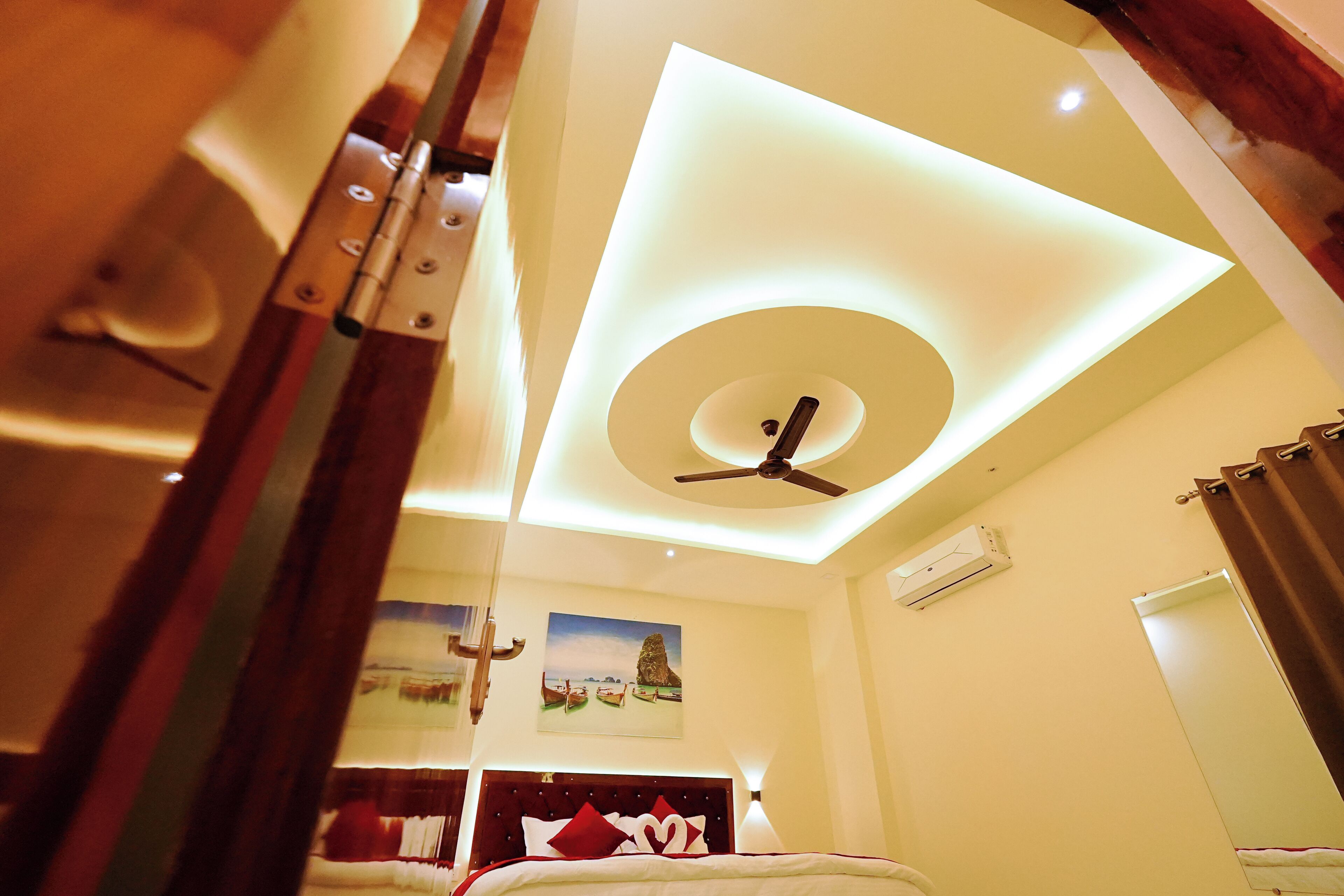 Une chambre d’hôtel avec un lit, un ventilateur de plafond, un climatiseur fixé au mur et un tableau représentant un paysage.