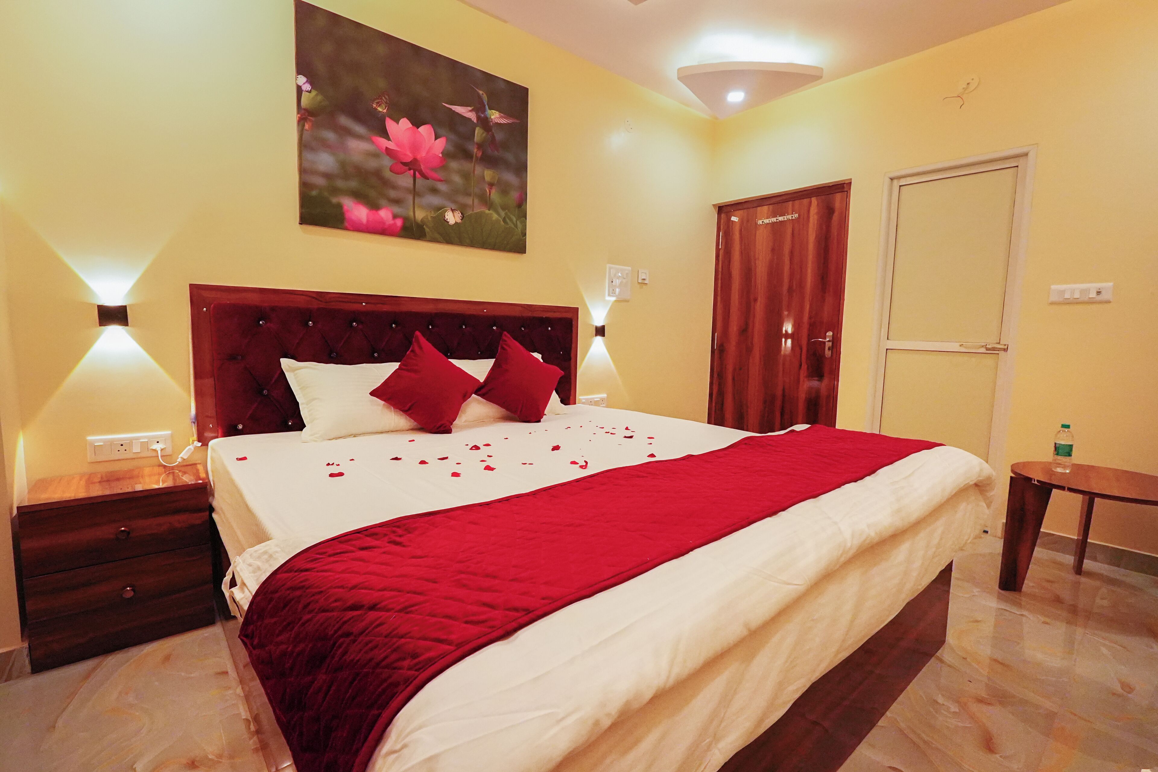 A neatly made bed with a red and white bedspread, a wooden headboard, and a wall-mounted painting of flowers.