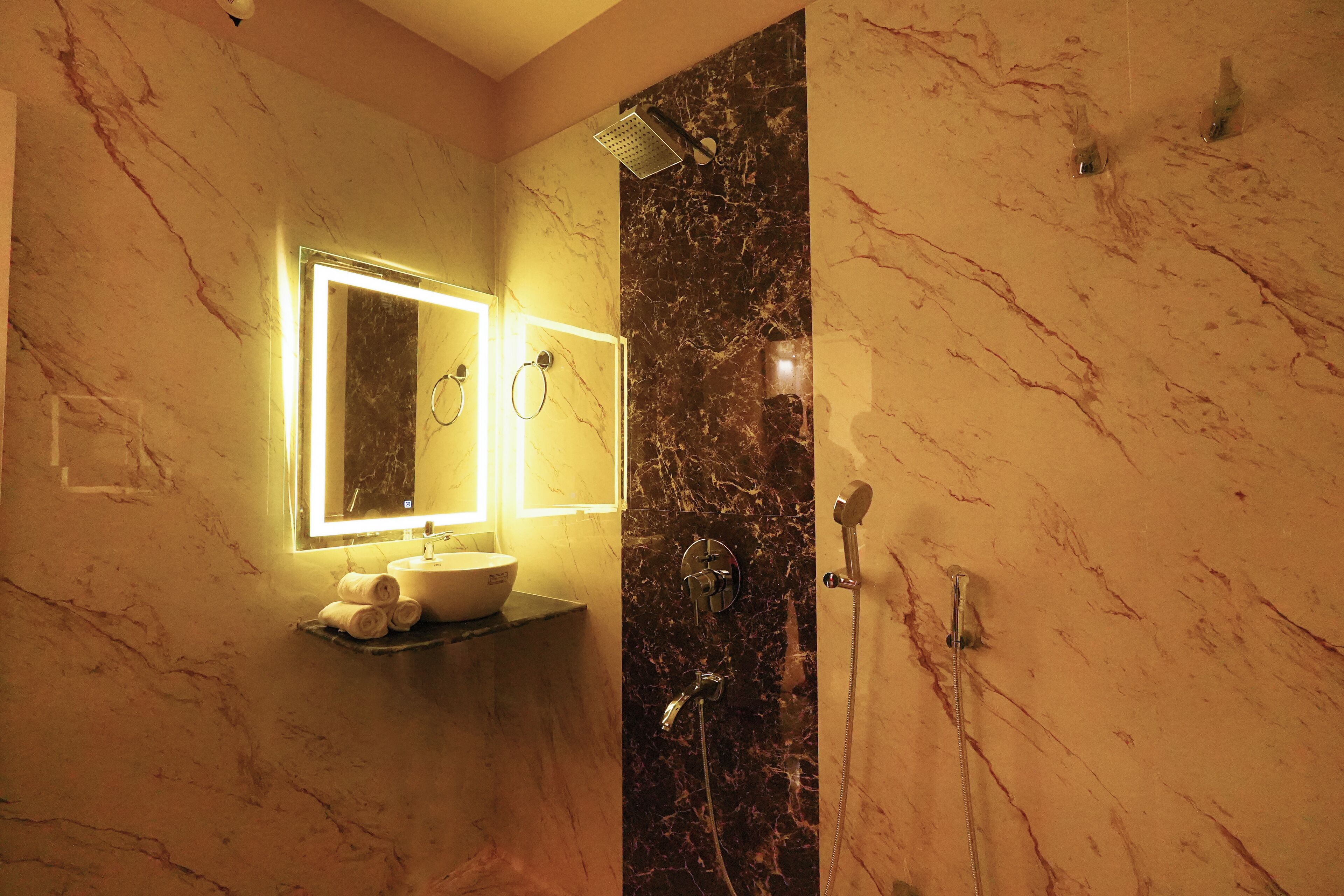 A bathroom with a marble wall, a sink with a mirror, and a shower.