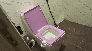 A bathroom with a toilet, a trash bin, and a toilet paper holder. - OHUNT HOMES (Abuja)
