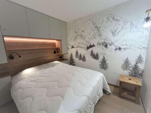 A bedroom with a bed, a wooden headboard, a wall mural of mountains, and a small wooden stool.
