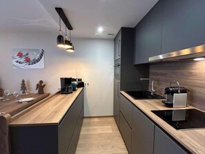 A modern kitchen with dark cabinetry, a wooden countertop, a built-in stove, and a coffee machine.