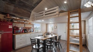 A kitchen with a wooden table, chairs, a refrigerator, and a ladder.