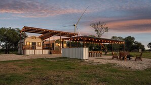 A rustic cabin with a covered patio, a wind turbine, and outdoor seating.