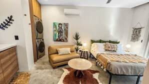 Een moderne slaapkamer met een bank, een ronde tafel, een bed met een gebloemd plaid en een wandairconditioner.