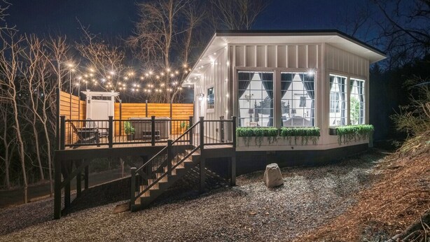 Una casa con porche techado, escaleras y terraza con luces de cuerda.