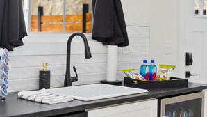 Una cocina moderna con un grifo negro, baldosas blancas, una encimera blanca y un ventanal con vistas a una valla de madera.