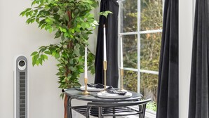 Una mesa de comedor con estructura metálica negra, una planta en maceta, una vela blanca y un mantel negro.