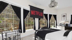 Un dormitorio moderno con una cama grande, un escritorio con una silla y una pantalla de televisión mostrando 