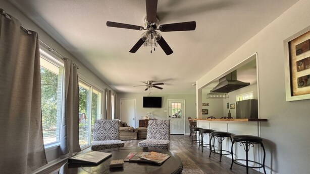 A spacious living room with a round coffee table, patterned armchairs, a ceiling fan, and a view of the kitchen through an open doorway. - Sleeps 10. Bayou Front Home close to ULM, Sports Complexes, Airport and I-20. (Monroe)