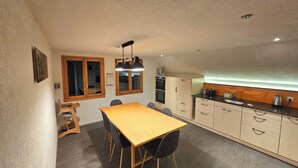 Eine kleine Küche mit Holztisch und Stühlen, einem eingebauten Ofen und einer Arbeitsfläche mit Wasserkocher.