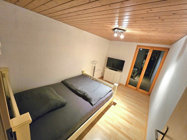 A bedroom with a bed, a television, and a sliding glass door.