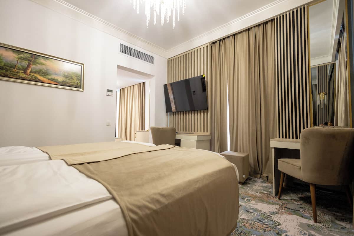 A hotel room with a large bed, a desk, a chair, a television, and a painting on the wall.