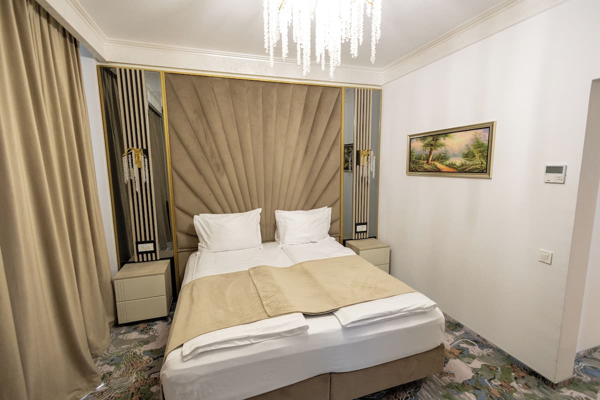A hotel room with a large bed, a bedside table, a nightstand, a mirror, and a painting on the wall.