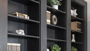 Une bibliothèque en bois foncé, dotée de plusieurs étagères, dont certaines contiennent des livres et des objets décoratifs, et d’autres abritent des plantes en pot.