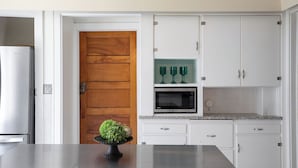 Une cuisine avec des meubles blancs, une porte en bois, un four à micro-ondes et une petite étagère avec des verres verts.