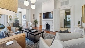 A spacious living room with a fireplace, a television mounted above it, and a large window. - Palazzo Sul Monte-Uno (Wilmington)