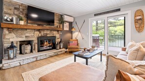 Un salon chaleureux avec une cheminée en pierre, un canapé confortable et une vue sur l’extérieur.