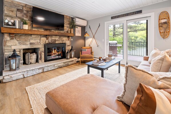 A cozy living room with a stone fireplace, a comfortable sofa, and a view of the outdoors. - Dog Friendly Lakefront Lodge with Private Beach (Newbury)