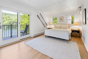 A bedroom with a bed, two bedside tables, a window, and a balcony with a chair. - Dog Friendly Lakefront Lodge with Private Beach (Newbury)