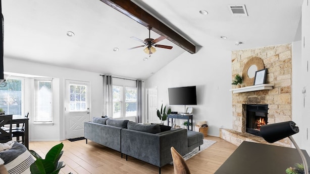 A spacious living room with a grey sofa, a flat-screen TV, a stone fireplace, and a ceiling fan. - Mini Golf | FirePit | GameRoom | 4BRs | Cedar Park (Cedar Park)