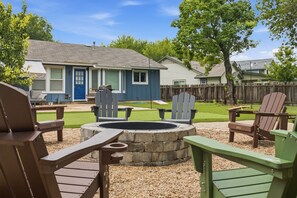 Un jardin avec un foyer, des fauteuils Adirondack et une maison en arrière-plan.