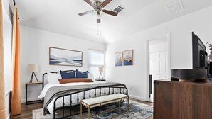 A bedroom with a bed, bedside tables, a bench, a ceiling fan, artwork on the walls, and a wooden dresser. - Mini Golf | FirePit | GameRoom | 4BRs | Cedar Park (Cedar Park)