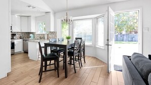 A modern kitchen with white cabinets, a dining area with a dark wooden table and chairs, and a view of the backyard through large windows. - Mini Golf | FirePit | GameRoom | 4BRs | Cedar Park (Cedar Park)