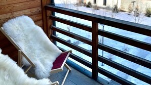 Un balcon avec deux fauteuils blancs à l’assise moelleuse, des murs en bois et une vue sur des maisons et des montagnes enneigées.