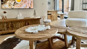 Un salon moderne avec une table basse en bois, un fauteuil blanc et un téléviseur fixé au mur.