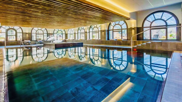 Une grande piscine intérieure dotée de fenêtres en arc de cercle et d’un plafond en bois.