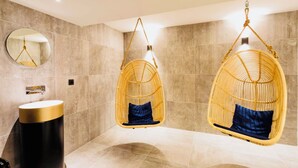 Une salle de bain moderne avec deux fauteuils suspendus en osier, un miroir rond et un lavabo aux tons dorés.