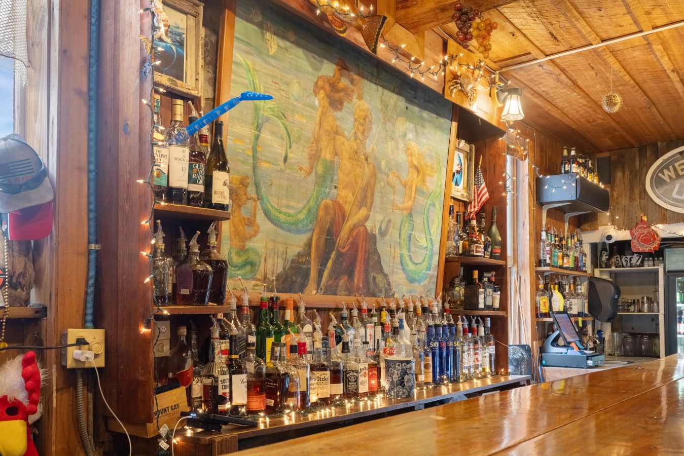 A bar area with a wooden ceiling, a mural, and shelves stocked with various liquor bottles.