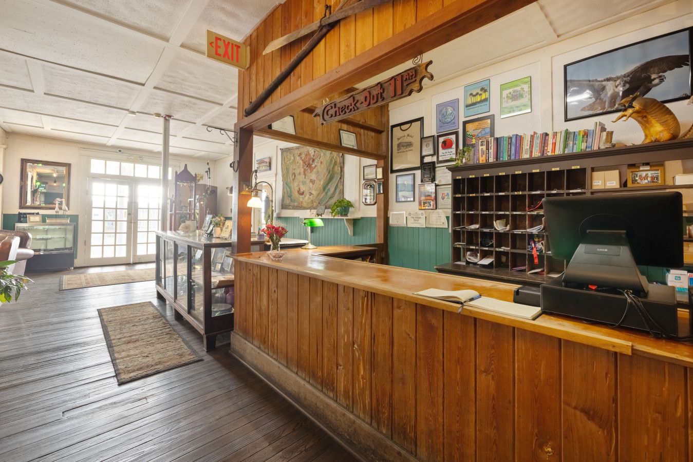 A reception desk with a wooden counter, a cash register, and a computer monitor. There are framed certificates on the wall, a map, and a shelf with books and a golden sculpture.