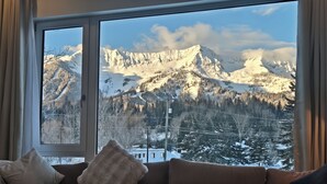 Ett vardagsrum med ett stort fönster som ger utsikt över snötäckta berg.