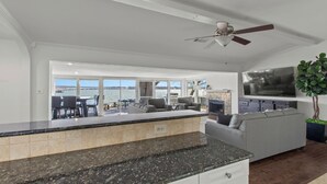 Una cocina moderna con encimera de granito, ventilador de techo y un televisor grande montado sobre el sofá.