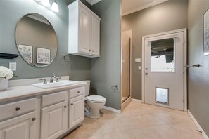 A bathroom with a white vanity, a toilet, a shower, and a door with a window.