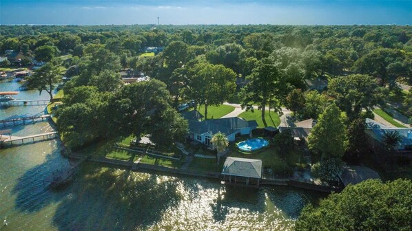 An aerial view of a residential area with houses, a swimming pool, and a dock extending into a body of water.