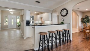 Una cocina amplia con una isla central, armarios blancos y un reloj en la pared.