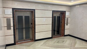 A hallway with two elevators, marble flooring, and recessed ceiling lighting. - DWC Residency (Kanchipuram)