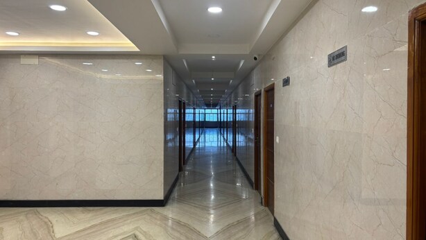 A modern hallway with marble floors and walls, recessed lighting, and a 'No Drinking' sign. - DWC Residency (Kanchipuram)